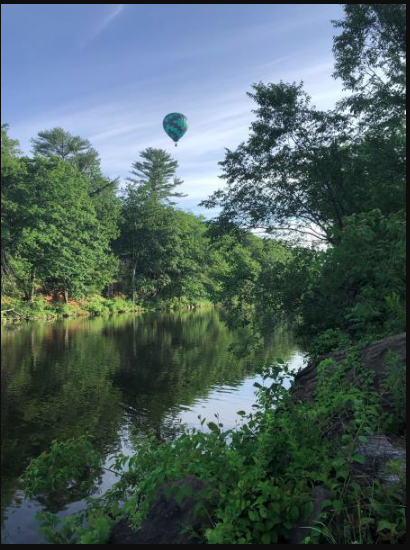 A colorful hot air balloon drifts above a serene river